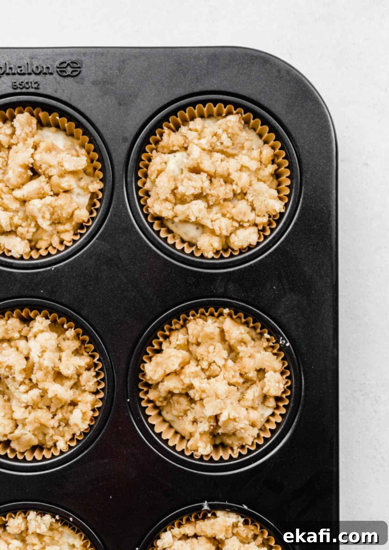 Ultra Moist Lemon Poppy Seed Muffins with Sour Cream 7 Crumb topping evenly sprinkled and gently pressed over Lemon Poppy Seed Muffin batter in a muffin tin, ready for baking.