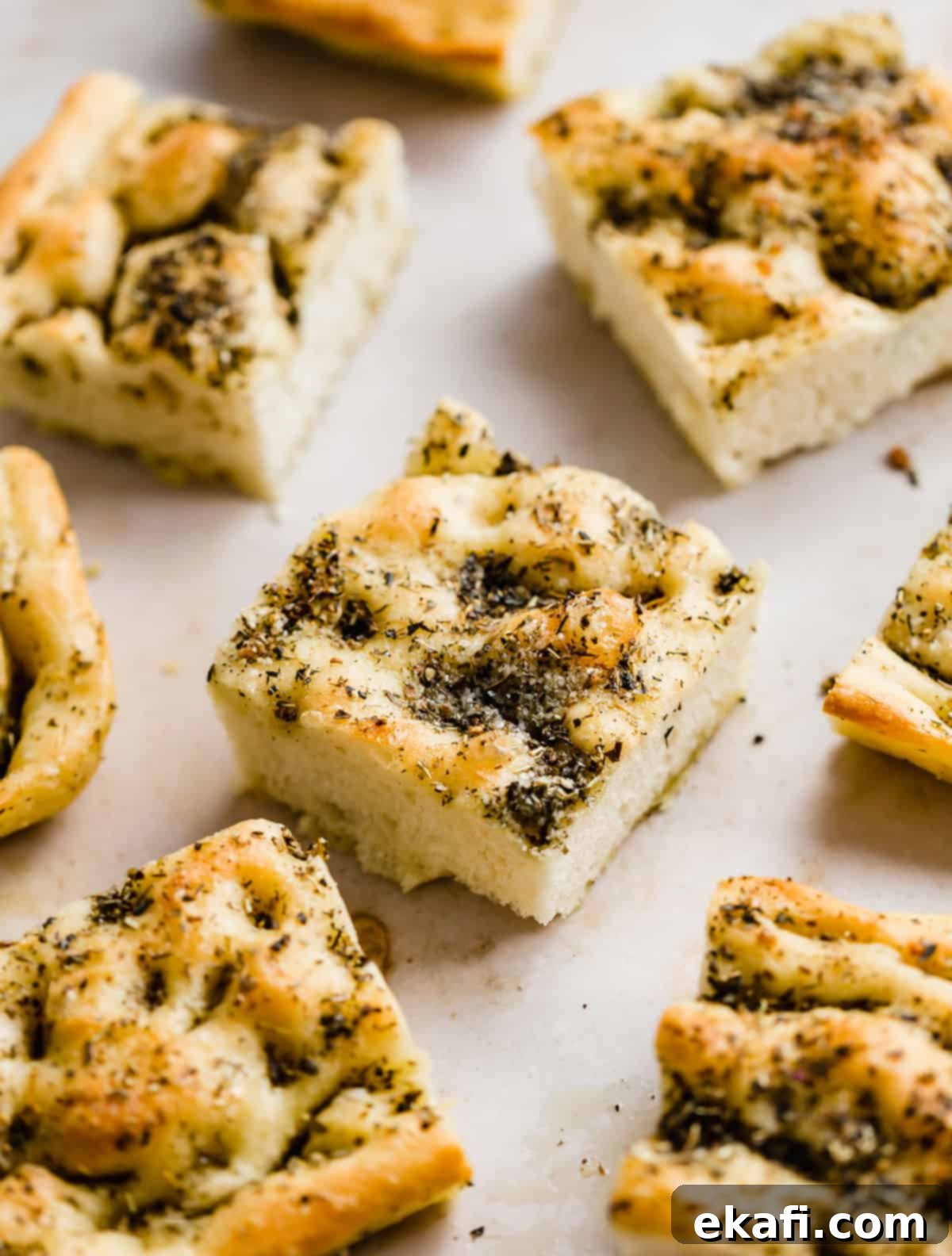 Artisanal Focaccia Bread 10 Focaccia Bread squares topped with fresh herbs on a light beige background.