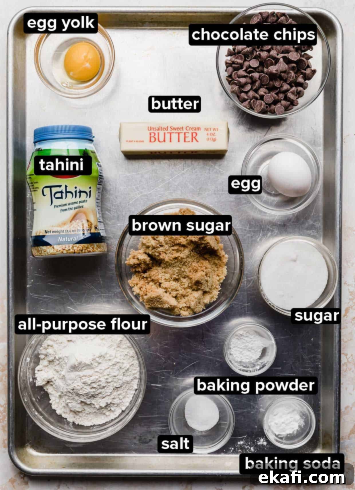 Sweet and Savory Tahini Chocolate Chip Cookies 3 Tahini Chocolate Chip Cookie ingredients portioned into glass bowls that are on a silver baking sheet.