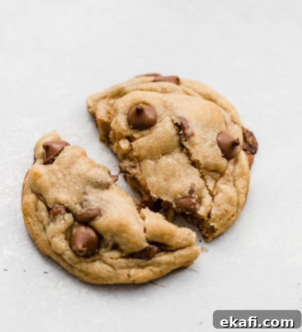 A homemade Crumbl chocolate chip cookie being torn in half, revealing its soft, gooey center.