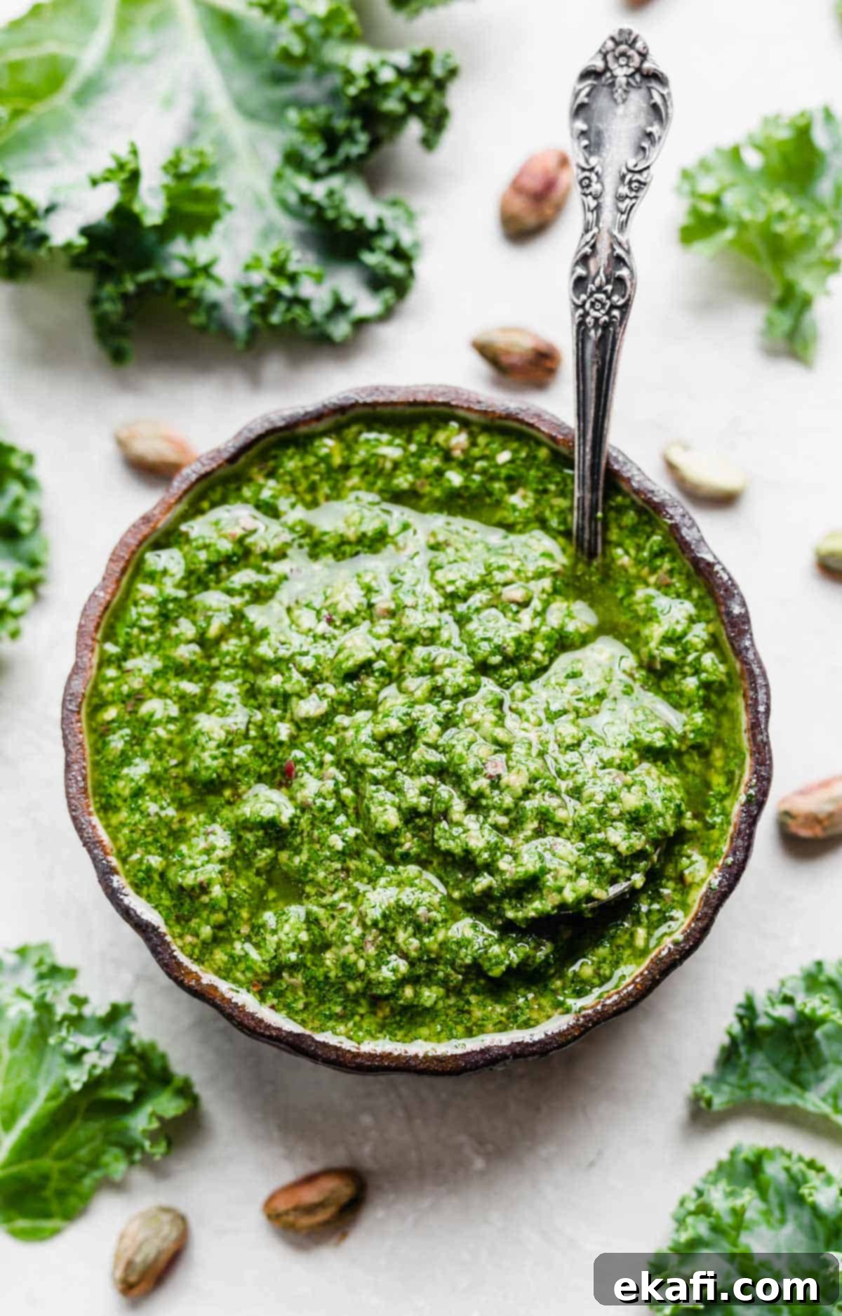 Easy Kale Pesto 2 Overhead photo of vibrant green Kale Pesto in a black bowl, garnished with whole pistachios.