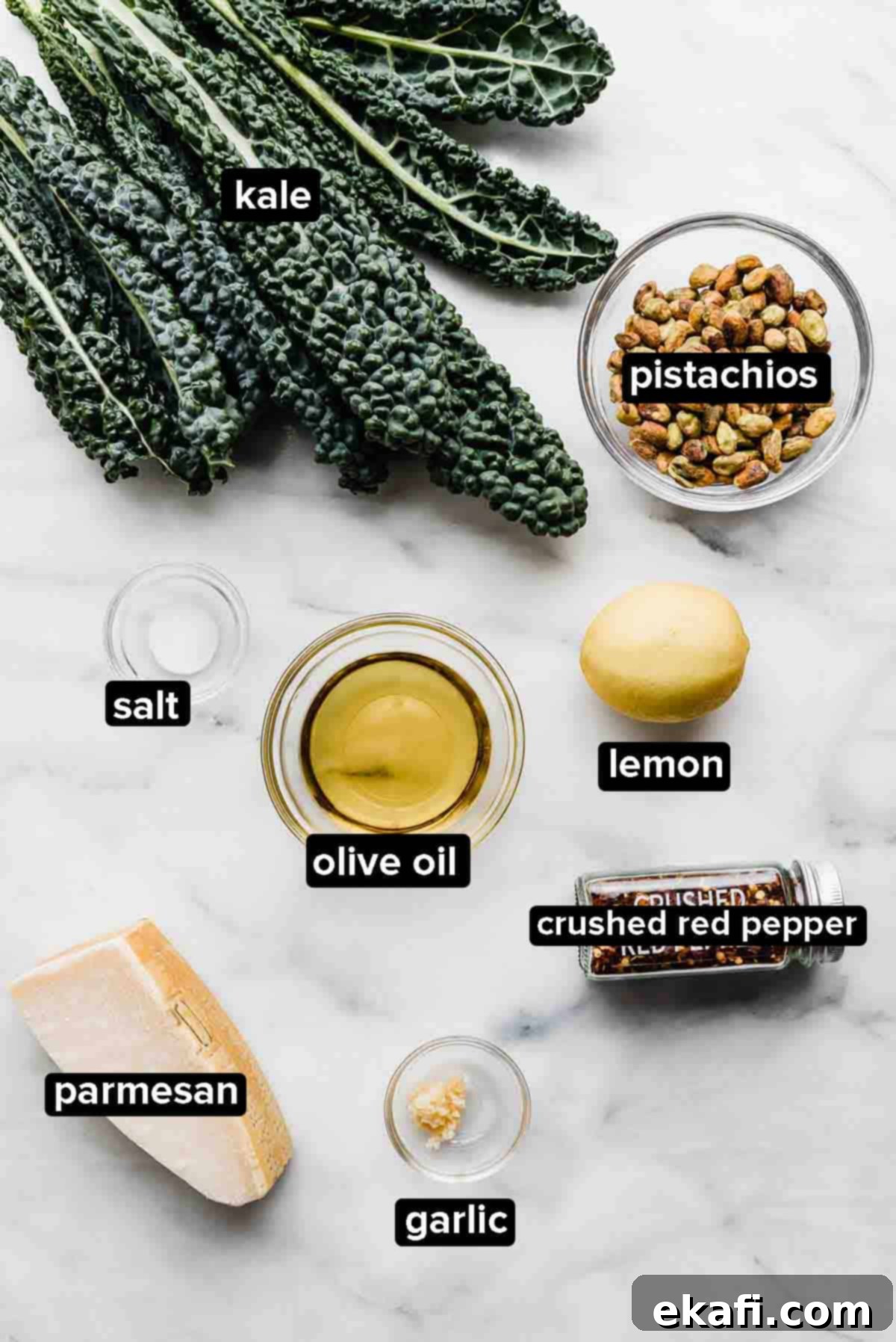 Easy Kale Pesto 3 Kale Pesto ingredients displayed on a white background: fresh kale, olive oil, pistachios, garlic cloves, and a block of parmesan cheese.