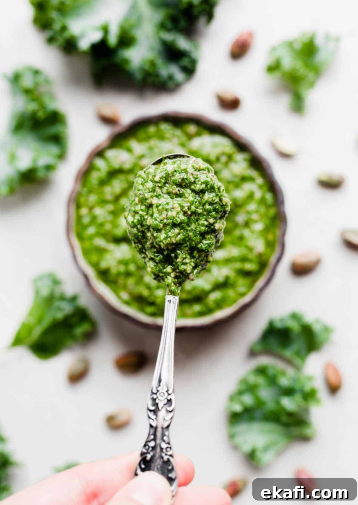 Easy Kale Pesto 5 A spoon lifting a spoonful of bright green Kale Pesto from a black bowl, showcasing its smooth texture.