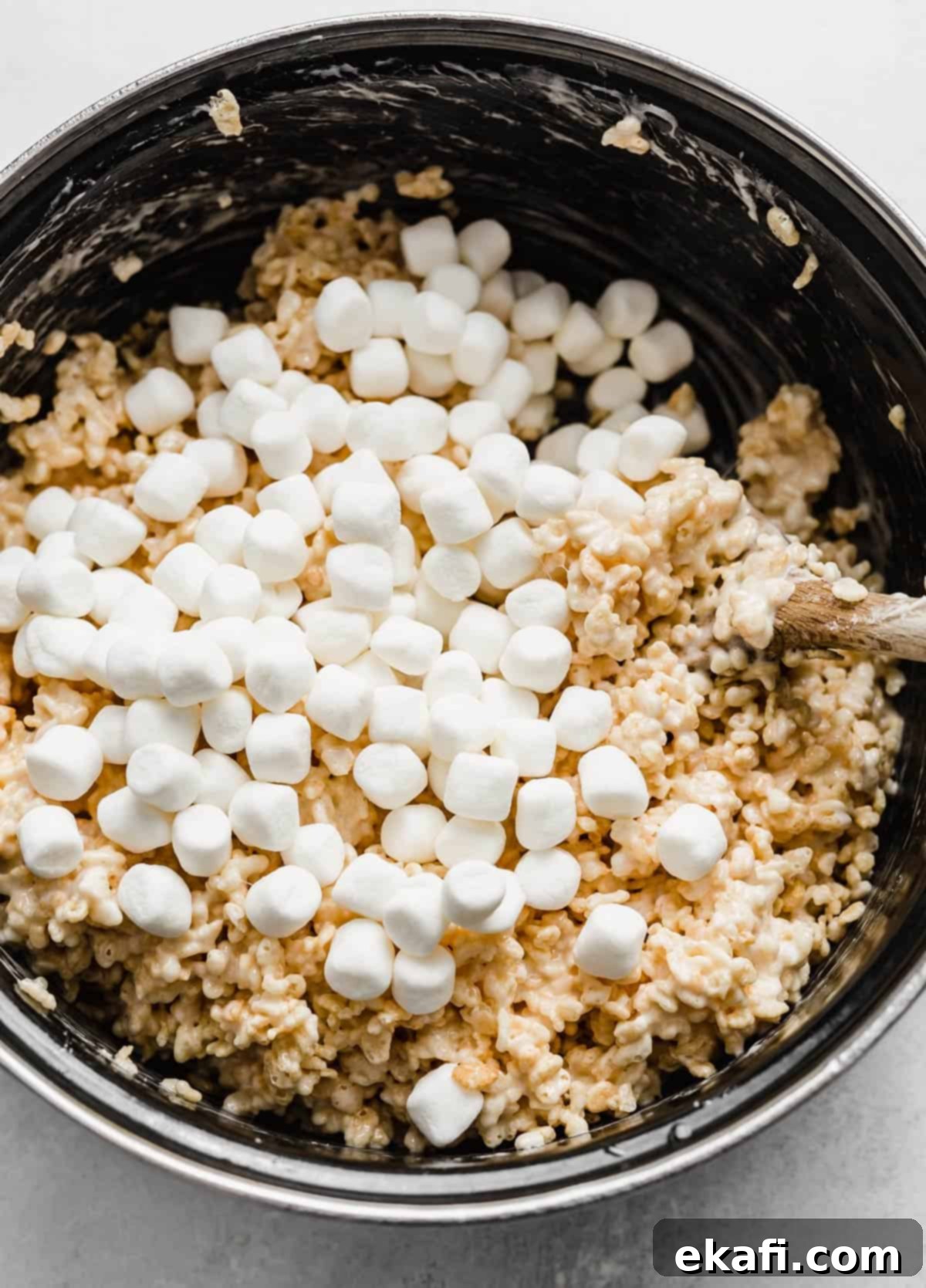 Ρυζοκροκέτες 7 Μίνι marshmallows ρίχνονται πάνω από ένα μείγμα Rice Krispies Treats σε μια μαύρη κατσαρόλα.