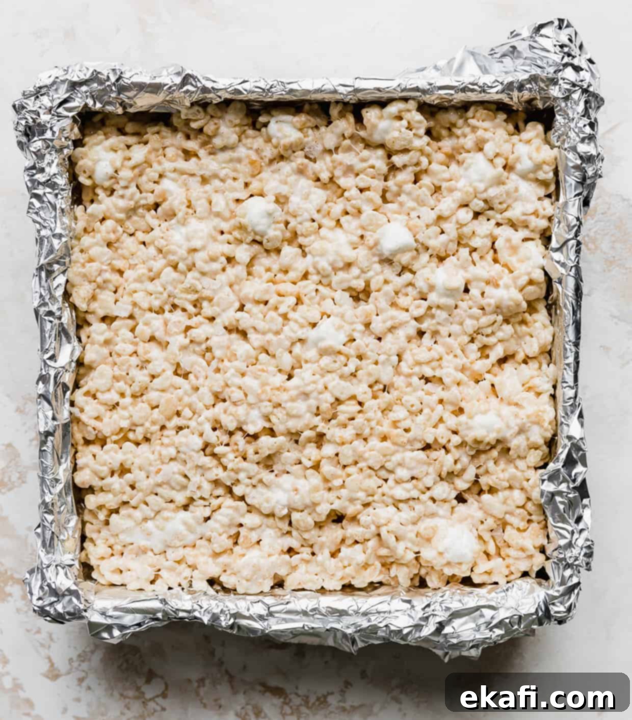 Ρυζοκροκέτες 9 Rice Krispie Treats με αλάτι και καφέ βούτυρο πιεσμένα σε ένα ταψί με αλουμινόχαρτο.