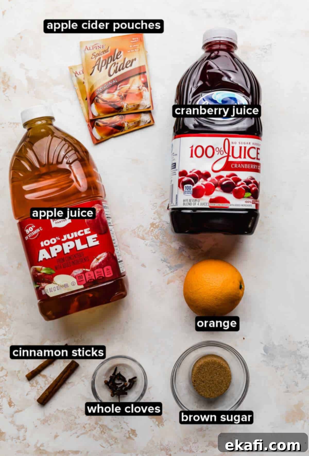 Spiced Cranberry Apple Cider 3 Cranberry Apple Cider ingredients on a white textured background: brown sugar, orange, cranberry juice, apple juice, spiced cider, cloves, and cinnamon sticks.