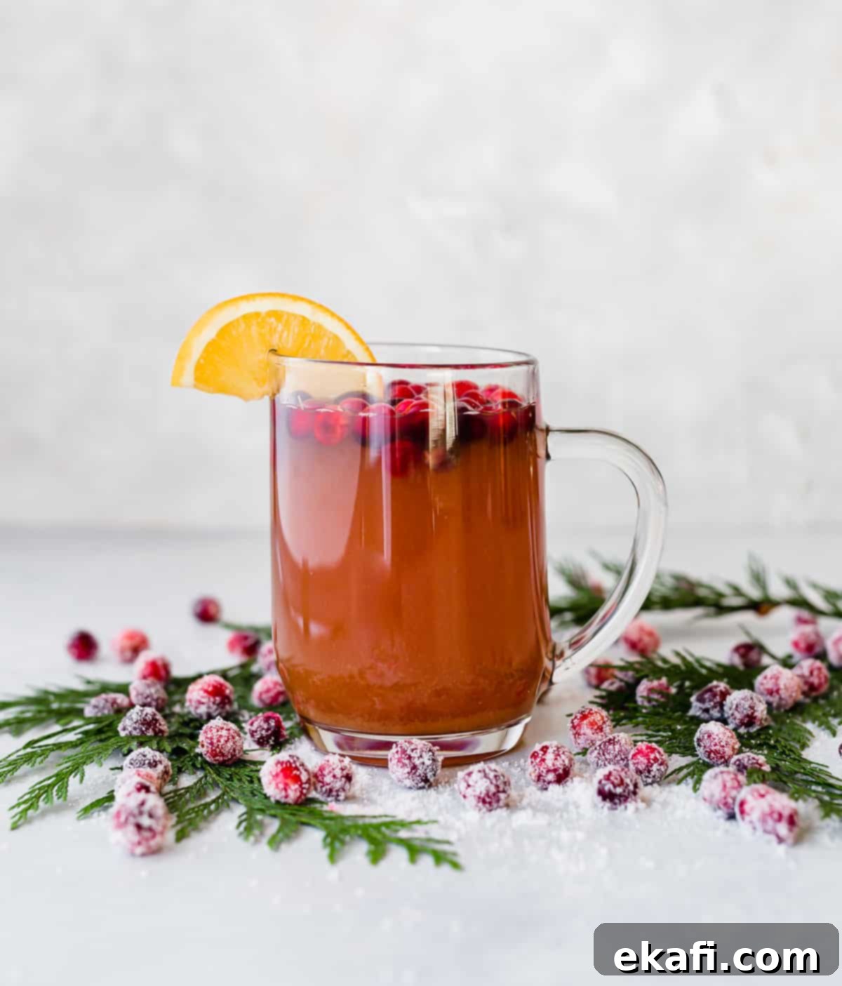 Spiced Cranberry Apple Cider 6 A glass mug filled with Cranberry Apple Cider against a white background with sugared cranberries on the table near the mug.