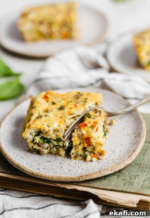 Effortless Breakfast Casserole 2 A fork cutting into a slice of breakfast casserole, showing layers of eggs, sausage, and vegetables.