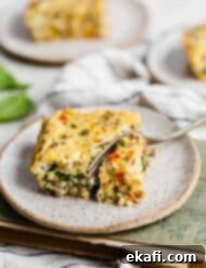 Effortless Breakfast Casserole 10 A fork cutting into a slice of breakfast casserole, showing layers of eggs, sausage, and vegetables.