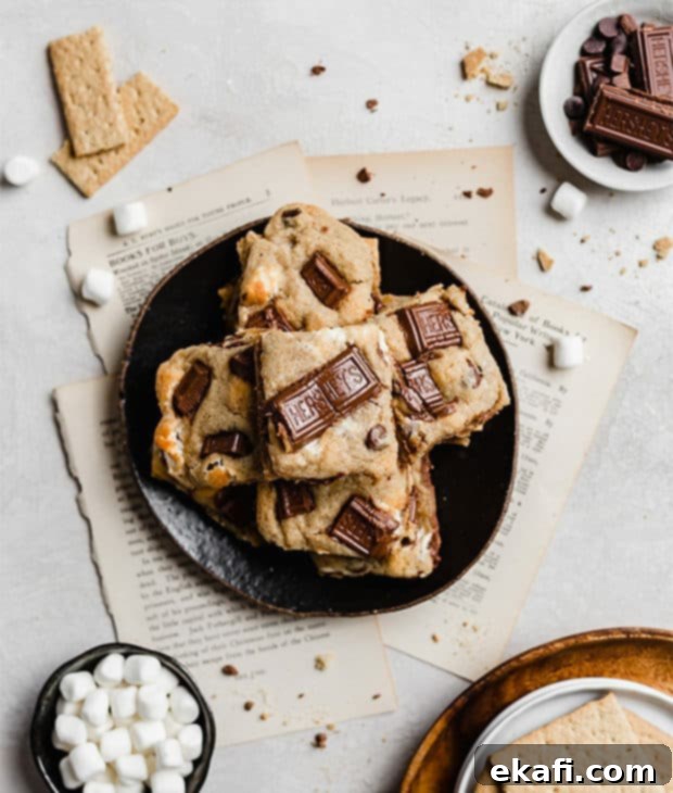 Smores Cookies 9 An inviting overhead photo of a plate brimming with freshly baked s'mores cookies, beautifully surrounded by the raw ingredients like marshmallows, graham crackers, and Hershey's chocolate bars, evoking a cozy campfire feel.