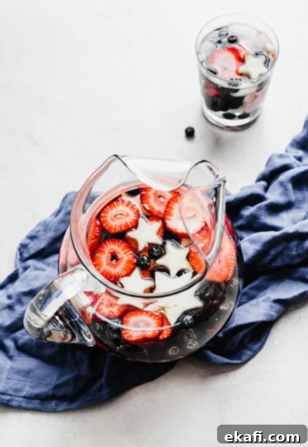 Red White and Blue Refresher 2 A glass pitcher full of sliced strawberries, blueberries, blackberries, and star shaped apples.