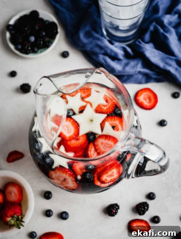 Red White and Blue Refresher 5 A glass pitcher full of sliced strawberries, blueberries, blackberries, and white apple stars.
