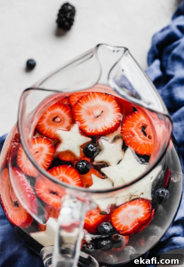 Red White and Blue Refresher 6 Close up of sliced strawberries, blueberries, and star shaped apples in a glass pitcher.