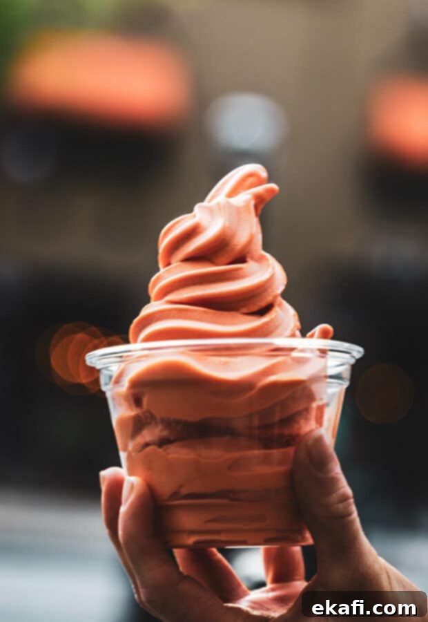 A hand holding a cup of pink/orange ice cream.