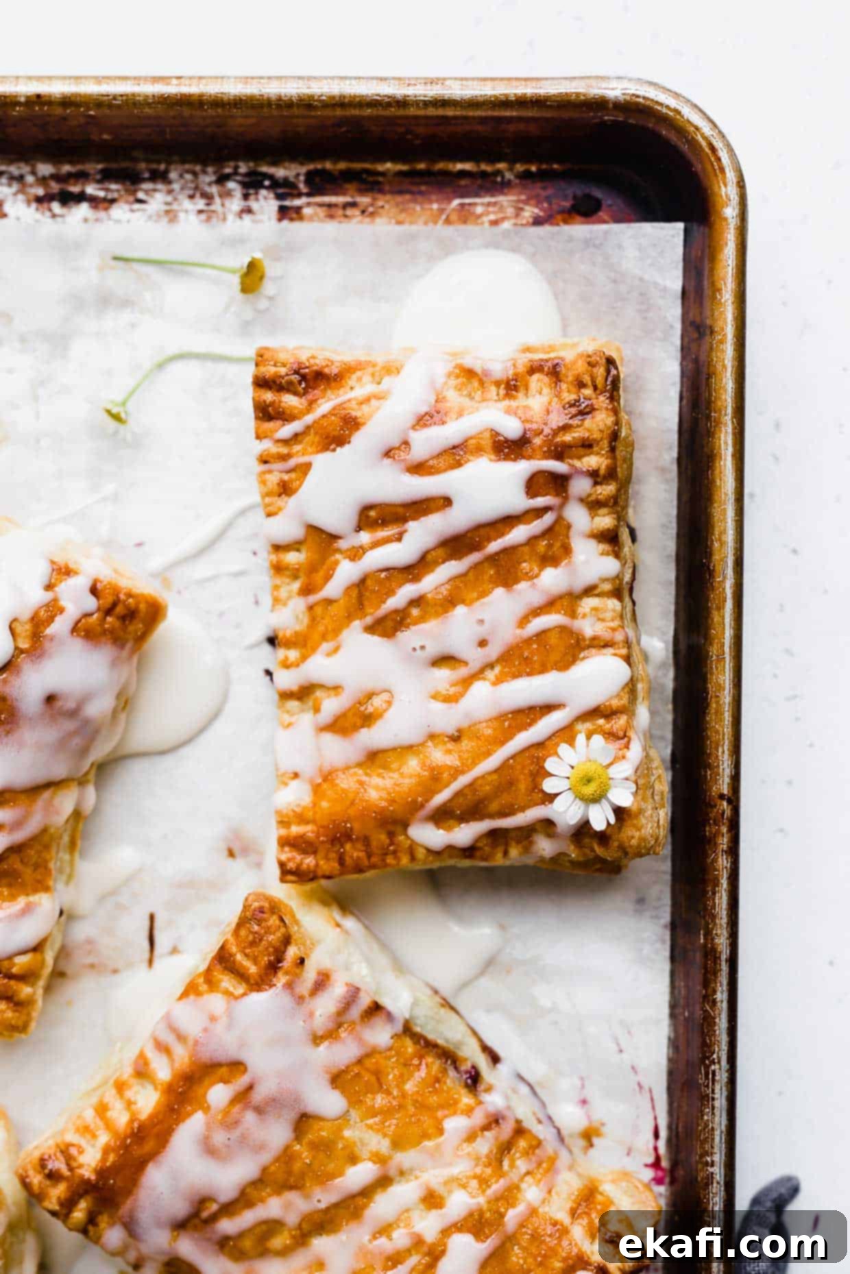 Σπιτικά Στρούντελ 8 Ένα Σπιτικό Triple Berry Toaster Strudels γεμάτο με μαρμελάδα και γαρνιρισμένο με λευκό γλάσο σε ένα ταψί.