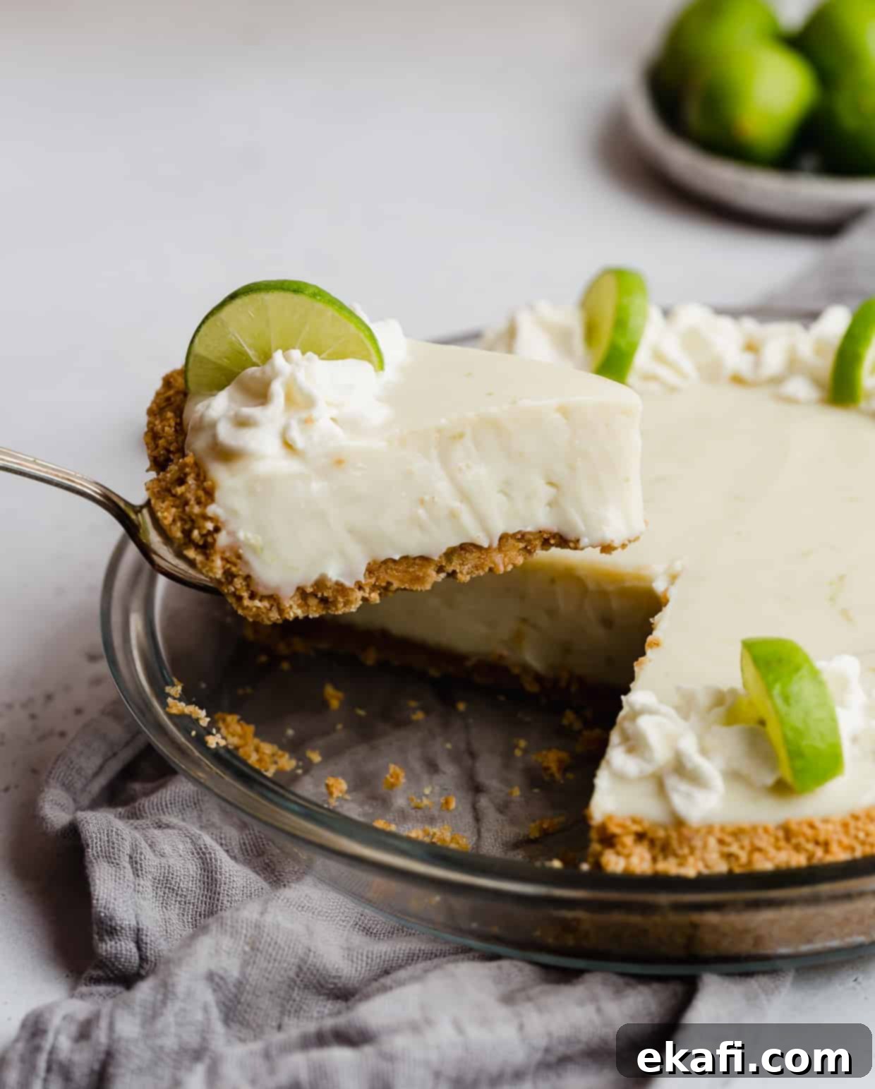 Velvety Key Lime Indulgence 2 A metal spatula holding up a perfectly golden slice of creamy Key Lime Pie with a luscious filling and graham cracker crust.