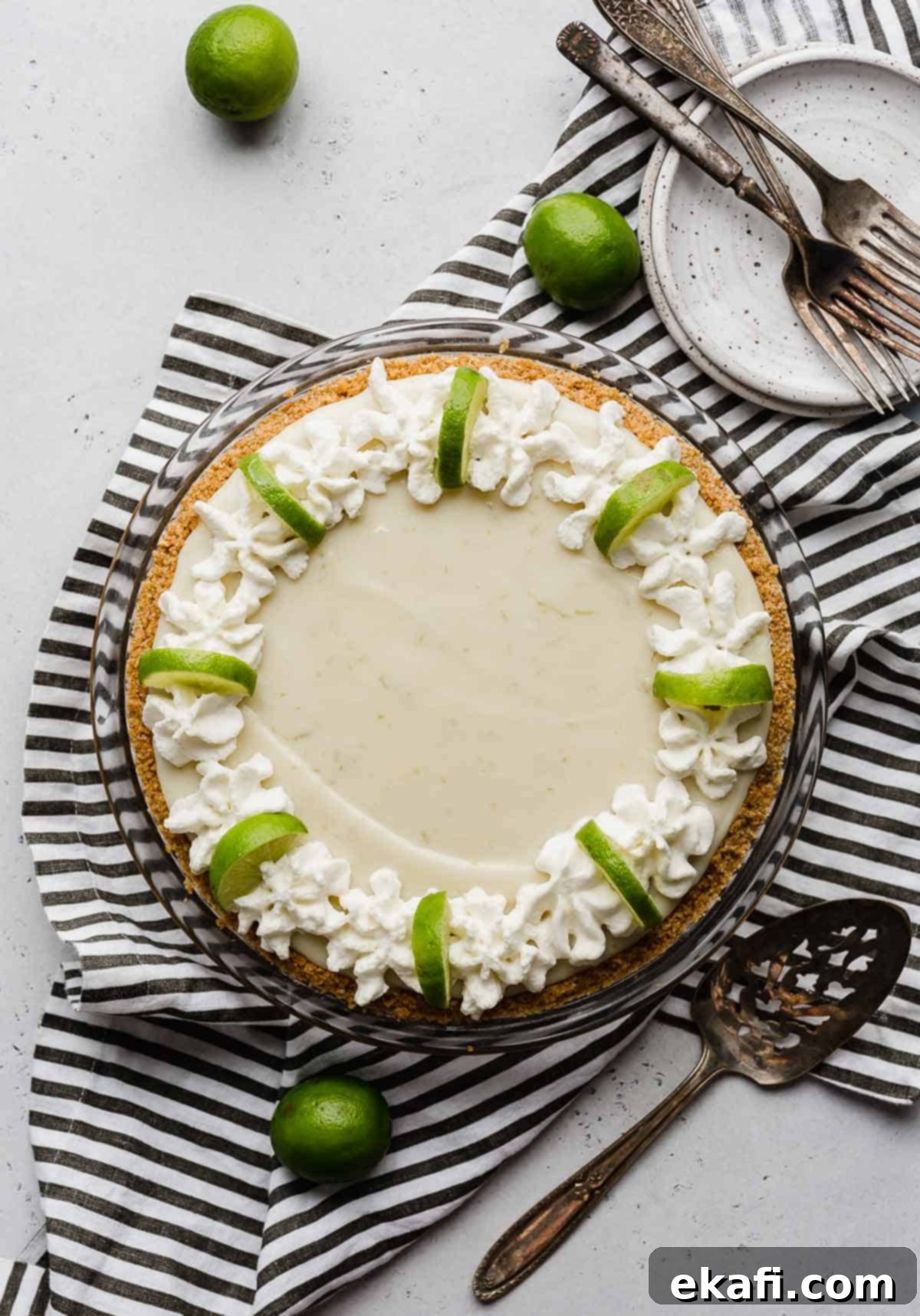 Velvety Key Lime Indulgence 5 An overhead shot of a luscious Key Lime Pie generously topped with homemade whipped cream swirls around the edges and fresh lime wedges for garnish.