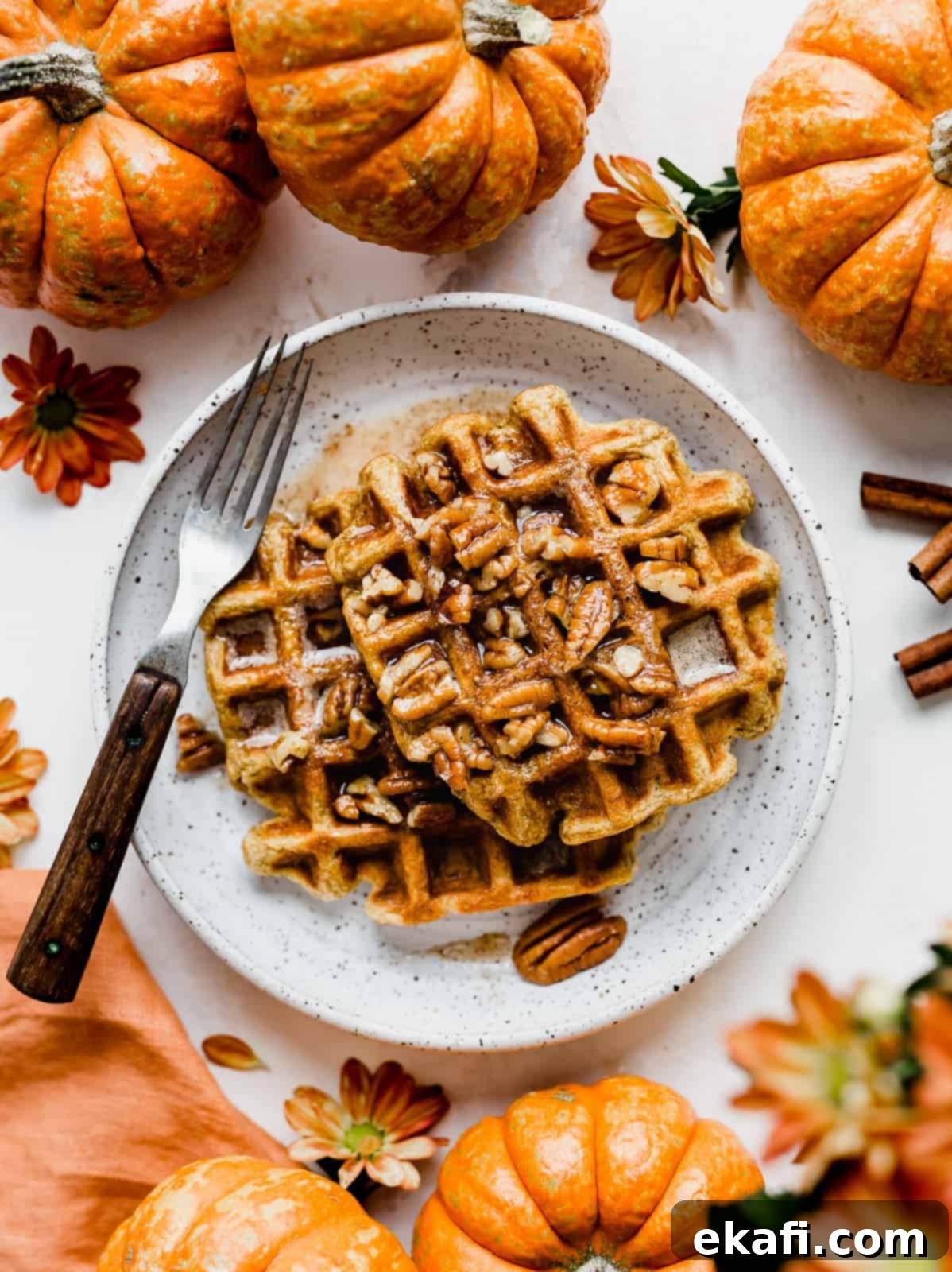 The Thirty-First Sweeter Wednesday 1 Two golden pumpkin waffles drizzled with syrup and surrounded by mini decorative pumpkins, resting on a white plate.