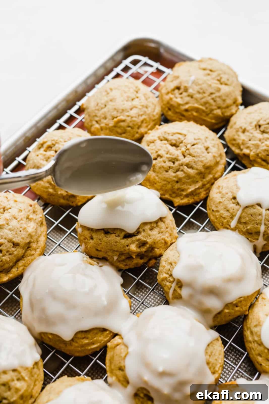 The Thirty-First Sweeter Wednesday 2 A spoon drizzling white glaze over a soft pumpkin cookie, highlighting its texture and inviting appearance.