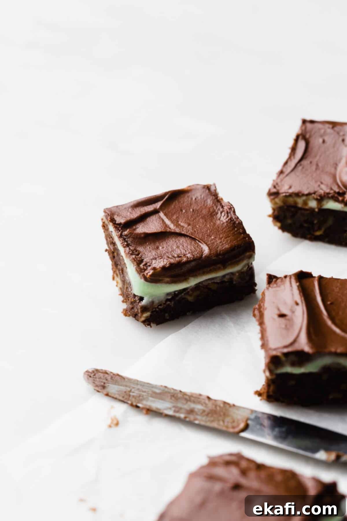 BYU Μπράουνις Μέντας 7 Ένα BYU Mint Brownie με γλάσο μέντας και σοκολάτας σε λευκό φόντο, με ένα μαχαίρι βουτύρου καλυμμένο με γλάσο δίπλα στο brownie.