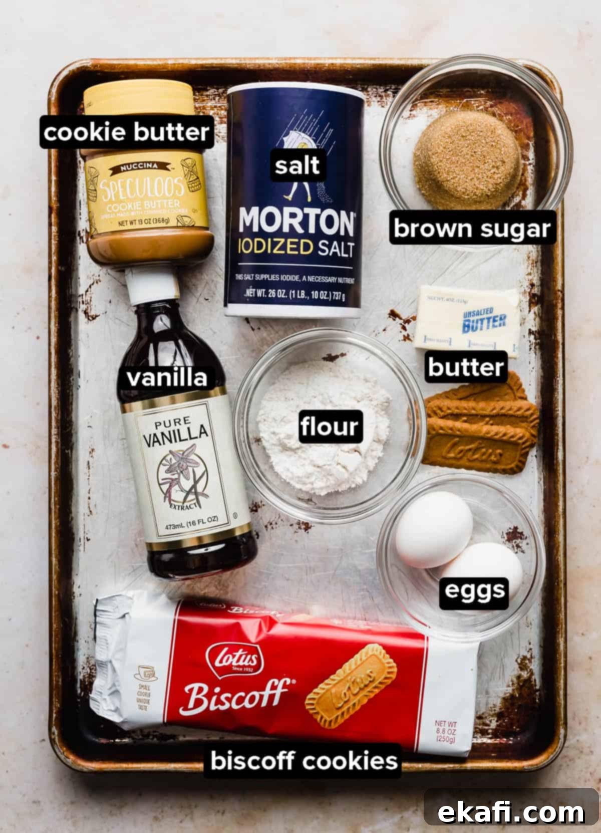 Μπράουνις Λωτού 3 Biscoff Brownies ingredients placed on a worn baking sheet on a white background.