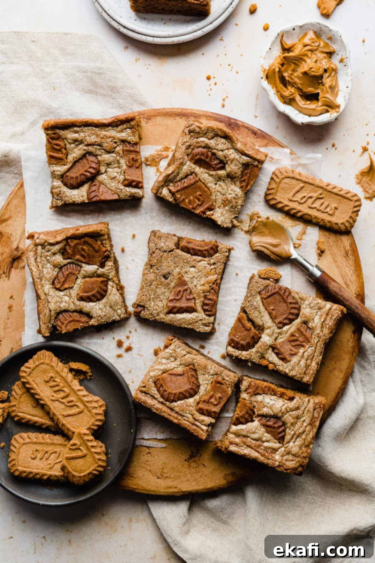 Μπράουνις Λωτού 6 Biscoff Brownies cut into squares resting on a white parchment paper that's on a brown round board.
