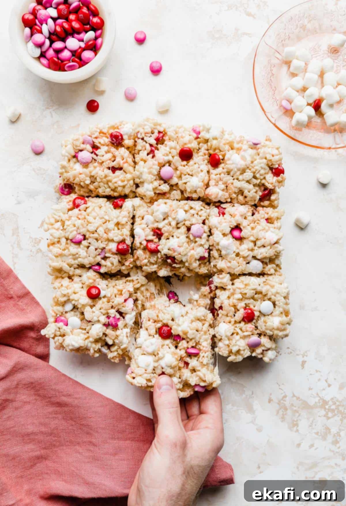 Colorful M and M Rice Krispie Bars 2 A hand grabbing a M&M Valentine Rice Krispie Treat showing the gooey marshmallow pulling.