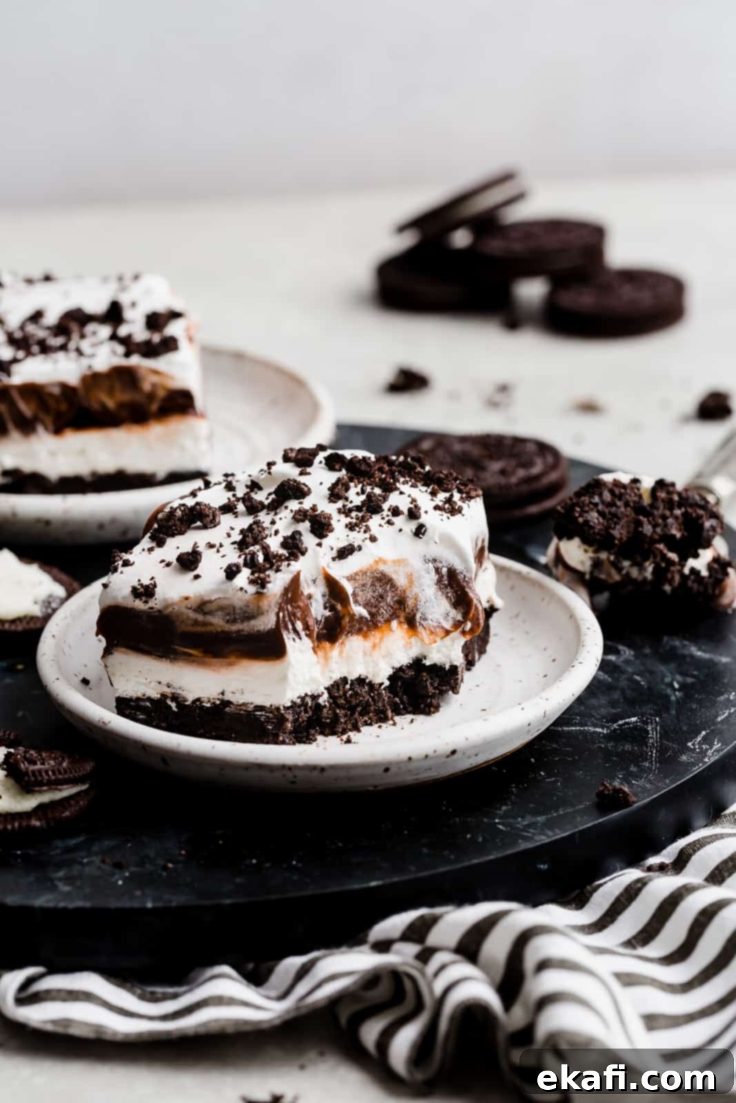 Effortless Oreo Magic 3 A oreo dessert on a white plate: Oreo crust, cream cheese filling, chocolate pudding, and whipped topping.