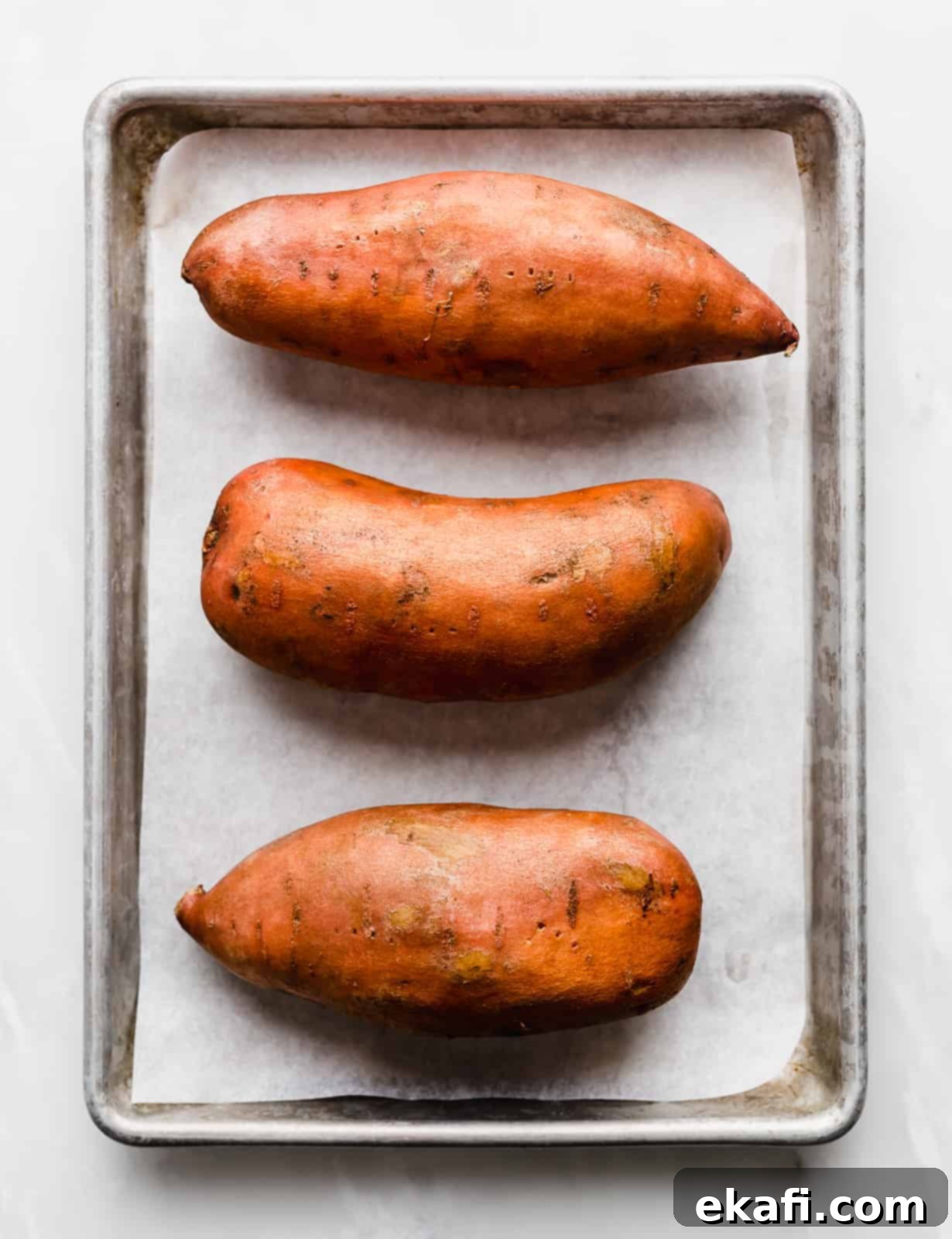 Easy Baked Sweet Potato 4 Three large sweet potatoes on a white parchment lined baking sheet.