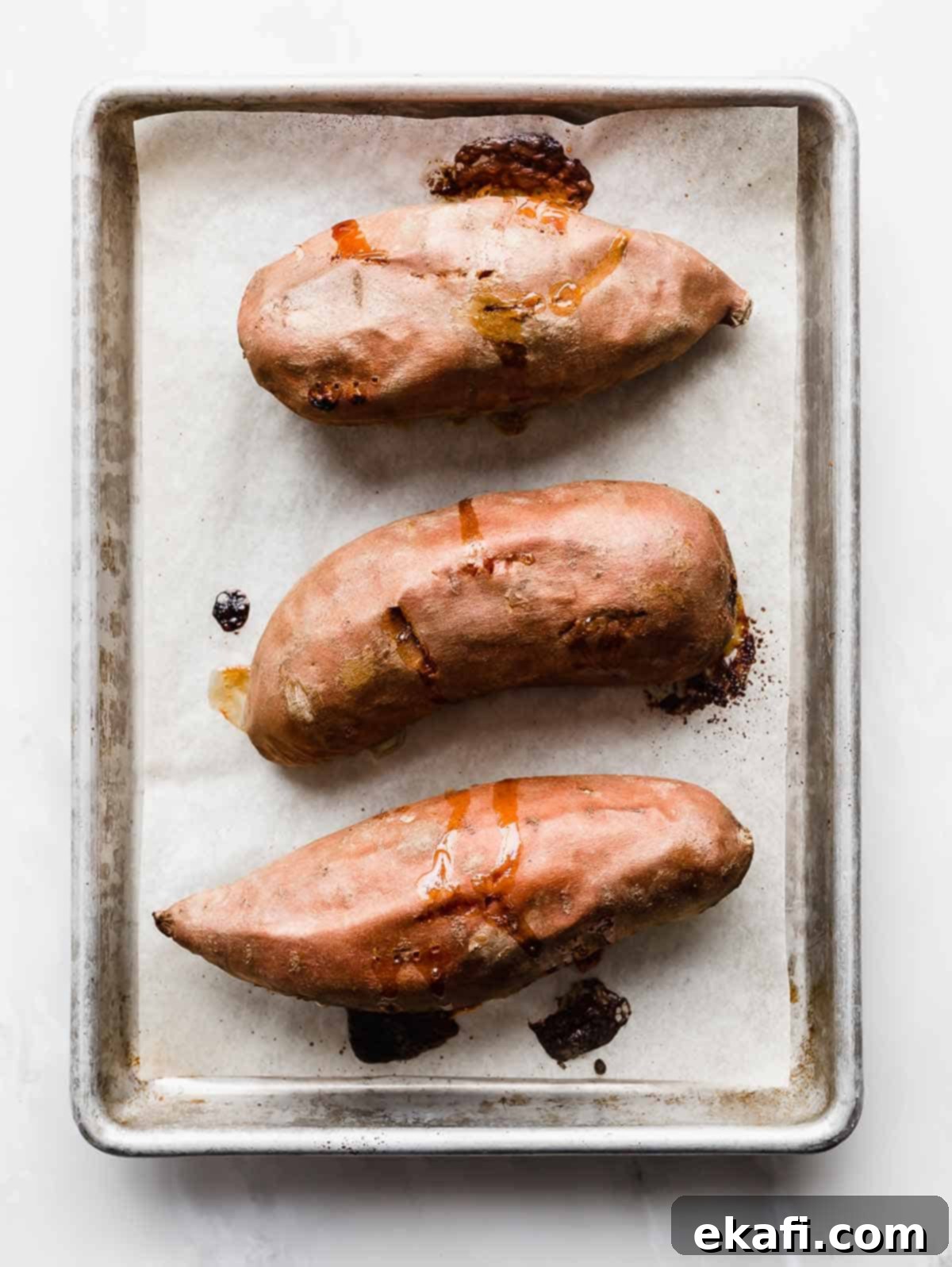 Easy Baked Sweet Potato 5 Three perfectly Baked Sweet Potatoes on a white parchment lined baking sheet.