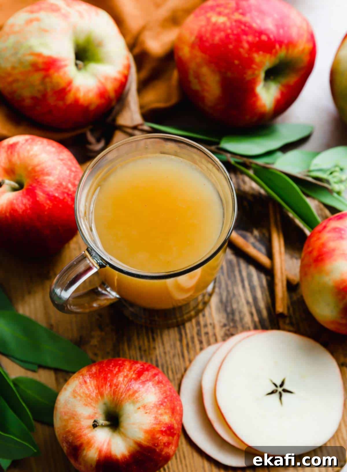Warm Yuletide Brew 5 Overhead photo of Hot Wassail in a clear mug with fresh apples and cinnamon sticks surrounding the mug on a rustic surface.