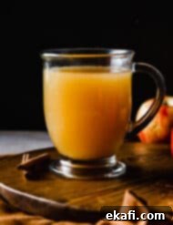 Warm Yuletide Brew 7 Hot Wassail recipe in a clear mug with apples next to the right of the mug.