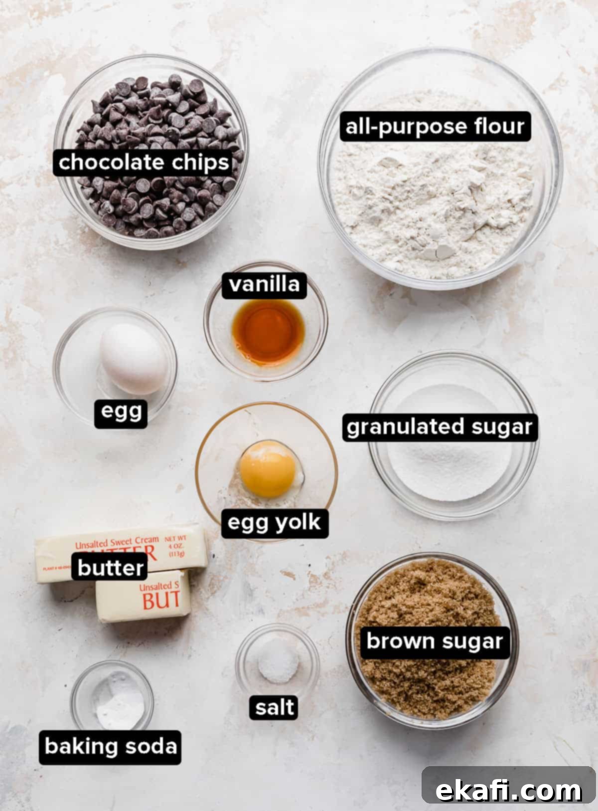 Decadent Chocolate Chip Cookie Bars 3 Chocolate Chip Cookie Bar ingredients, including melted butter, various sugars, eggs, flour, and chocolate chips, arranged in small glass bowls on a white textured background.