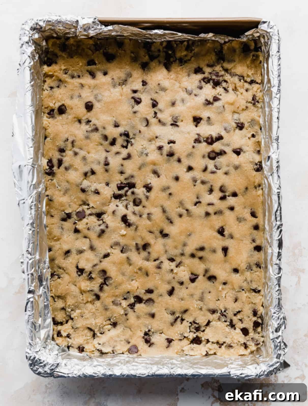 Decadent Chocolate Chip Cookie Bars 8 A 9x13 inch baking dish filled with unbaked chocolate chip cookie dough, evenly pressed and ready for the oven.