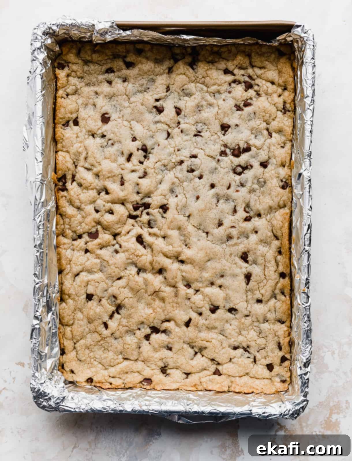 Decadent Chocolate Chip Cookie Bars 9 Freshly baked Chocolate Chip Cookie Bars cooling in a foil-lined 9x13 inch pan, showcasing their golden-brown edges.