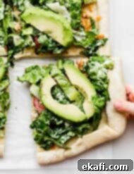 CPK Καλιφόρνια Κλαμπ Πίτσα 9 Ένα μικρό χέρι πιάνει ένα τετράγωνο κομμάτι CPK Club pizza με μαρούλι από πάνω.