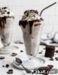 Ultimate Oreo Indulgence 8 Two milkshake glasses filled with the best Oreo Milkshake recipe, against a white brick background with Oreo crumbs scattered around the cups.