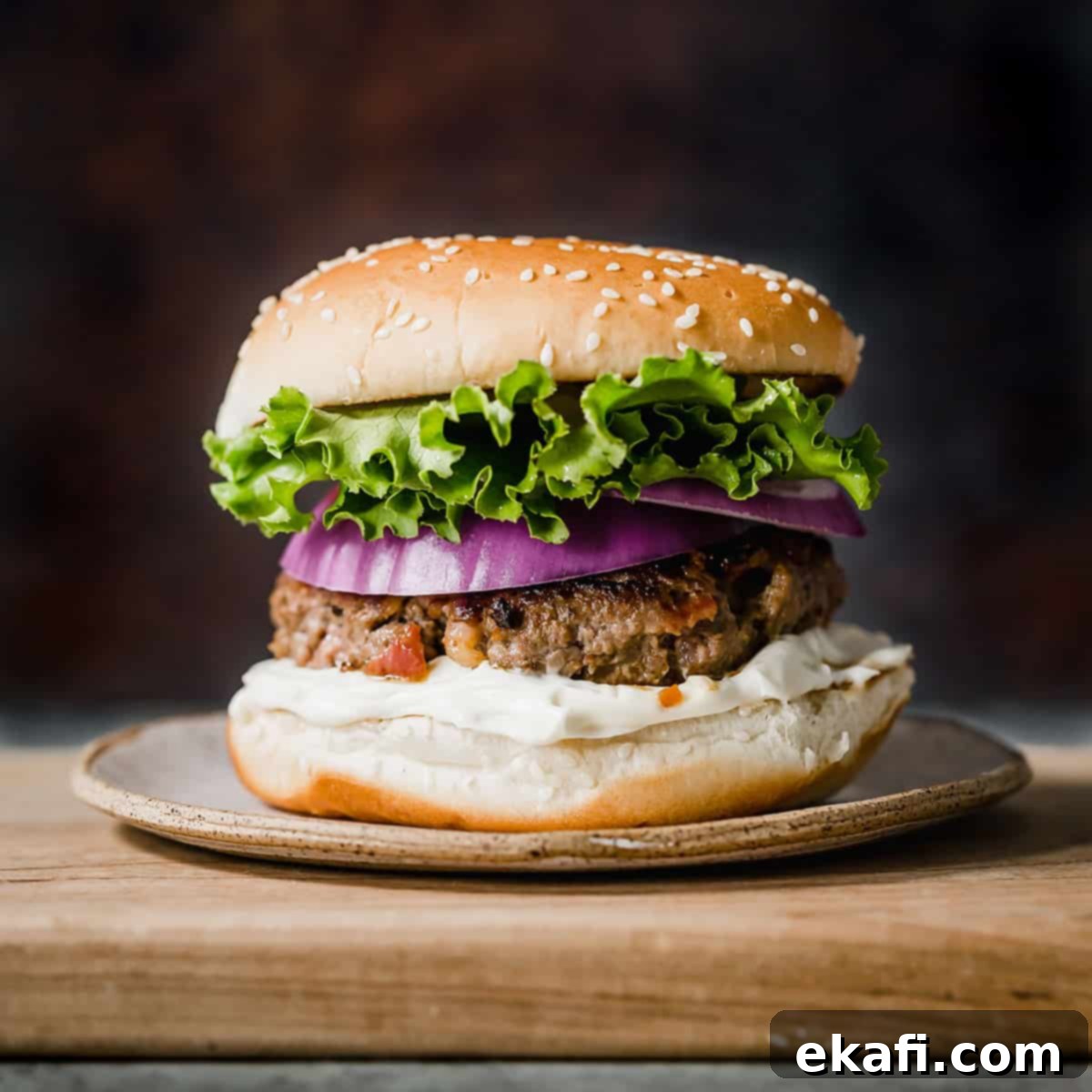 Gridiron Grub 24 A bacon burger on a cutting board with green lettuce and purple onion on the burger.