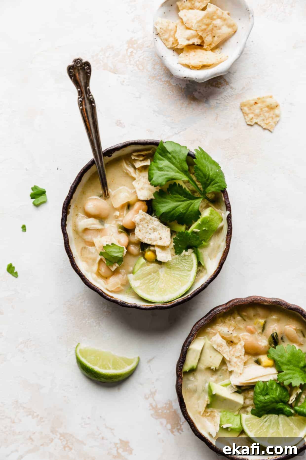 Creamy White Chicken Chili 7 A bowl of Best White Chicken Chili against a white background, topped with fresh cilantro, a lime wedge, and crunchy tortilla chips.