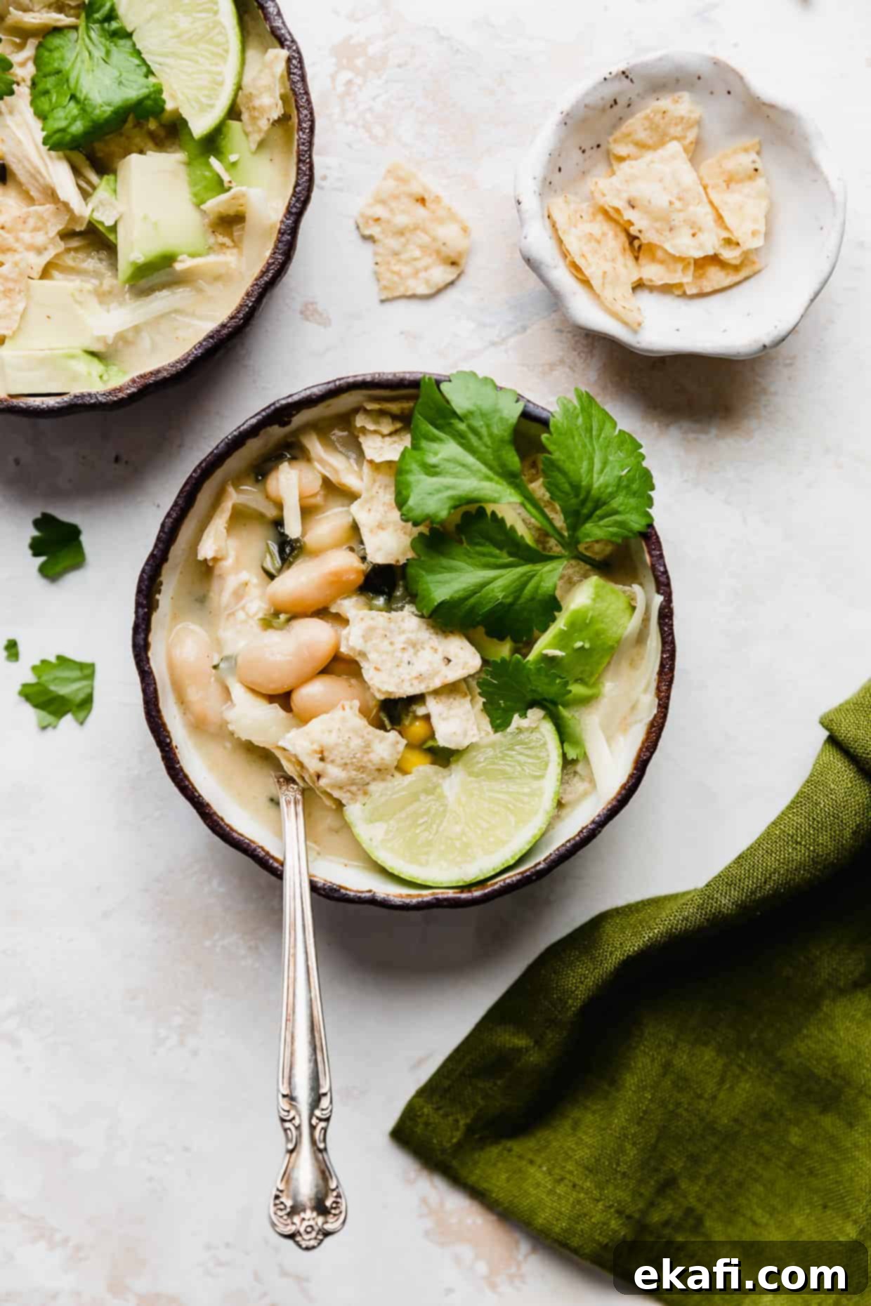 Creamy White Chicken Chili 8 A small bowl of creamy white chicken chili with a spoon, against a pristine white background.