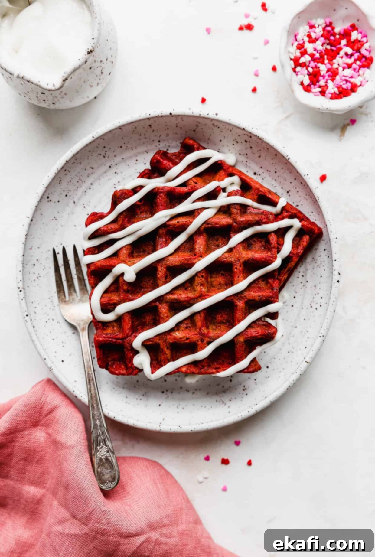 Velvet Dream Waffles 2 A white plate with 2 red velvet waffles on it drizzled in a white cream cheese glaze, against a white background.