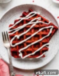 Velvet Dream Waffles 11 Two Red Velvet Waffles that are drizzled with a cream cheese glaze, on a white plate.