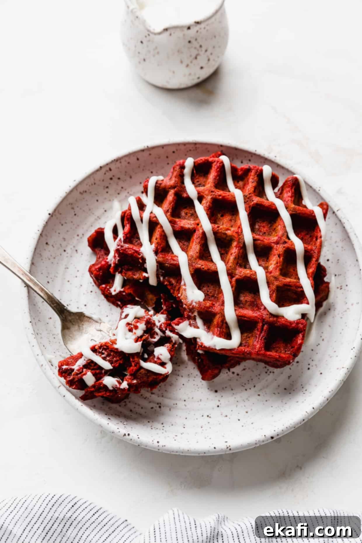 Velvet Dream Waffles 10 Two red velvet waffles drizzled with a white glaze on a white plate, against a white background.