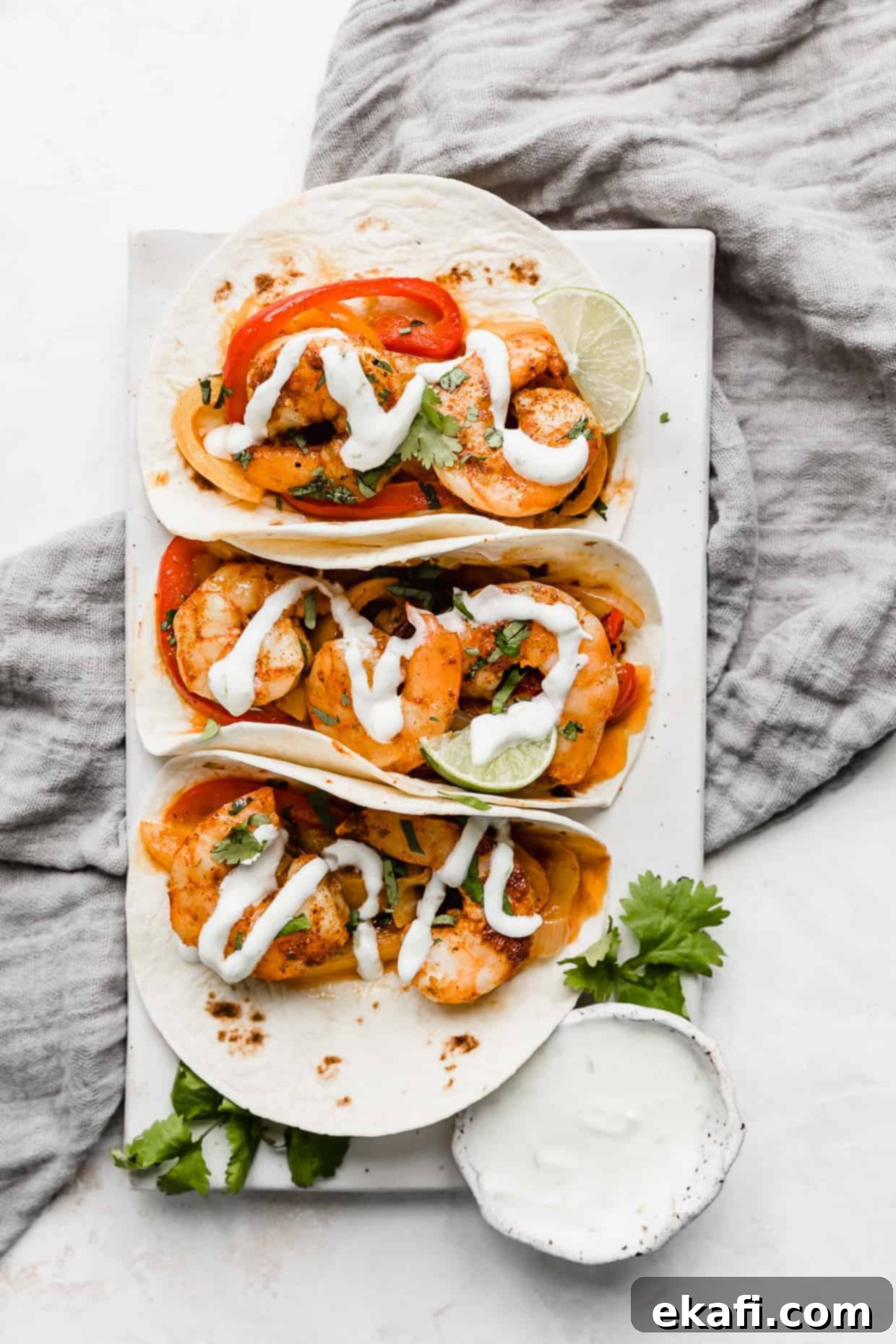One-Pan Shrimp Fajitas 8 Shrimp fajitas on a white rectangle plate resting on a grey linen napkin.