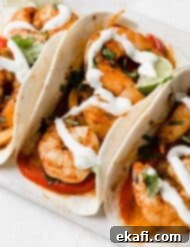 One-Pan Shrimp Fajitas 9 Sheet Pan Shrimp Fajitas drizzled with white Lime Crema on a white plate and white background.